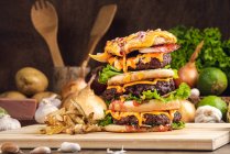 Hamburgers appétissants aux légumes placés sur une planche de bois avec frites dans la cuisine — Photo de stock