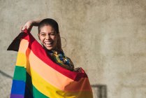 Contenuto giovane donna etnica bisessuale con bandiera multicolore che rappresenta i simboli LGBTQ che guardano dall'alto in basso nella giornata di sole — Foto stock