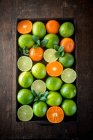 From above of ripe green limes and oranges placed in box on wooden rustic table — Stock Photo
