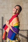Zufriedene junge bisexuelle ethnische Frau mit bunter Flagge, die LGBTQ-Symbole darstellt und an sonnigen Tagen in die Kamera blickt — Stockfoto