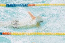Vue latérale du sportif paralympique en lunettes et casquette sans nage à la main style rampant dans la piscine entre les voies — Photo de stock
