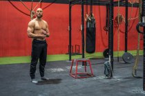 Ganzkörperkräftiger bärtiger Mann, der wegschaut und denkt, während er beim Training in einem modernen Fitnessstudio in der Nähe von Geräten steht — Stockfoto