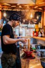 Vista laterale dell'uomo in bandana in piedi al bancone e il ramen di cottura nel moderno caffè asiatico — Foto stock