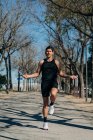 Atleta masculino em sportswear pulando com corda e olhando para longe na passarela durante o treinamento cardio no parque — Fotografia de Stock