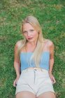 From above tranquil female in summer outfit sitting on green meadow in garden and looking at camera — Stock Photo