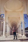 Positive young Asian female in colorful traditional headscarf smiling and looking away while standing near beautiful white building of Al Rahma Mosque in Jeddah in Saudi Arabia — Stock Photo