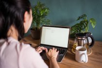 Back view of unrecognizable Asian female freelancer reading documents on laptop while sitting at table during remote work — Stock Photo