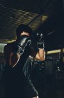 Junger fokussierter asiatischer Mann beim Boxtraining, während er mit schwerem Boxsack in einem modernen Fitnessstudio trainiert — Stockfoto