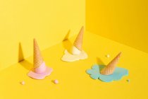 Мокап синий, желтый и розовый таяние мороженого в вафельный конус помещен на желтый фон, представляющий летнюю концепцию — стоковое фото