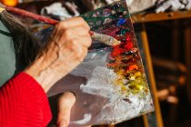 Сверху неопознаваемая старшая художница смешивает цвета на палитре красок в художественной мастерской — стоковое фото