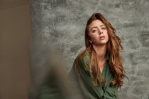 Niedriger Winkel der attraktiven Frau mit langen Haaren, die Kamera auf grauem Hintergrund im Studio anschaut — Stockfoto
