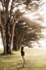 Full body of female traveler enjoying sunbeams penetrating lush branches of cypress trees on meadow of alley in Point Reyes park — Stock Photo