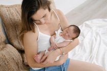 From above delicate mother sitting with adorable infant on soft bed in cozy room at home — Stock Photo