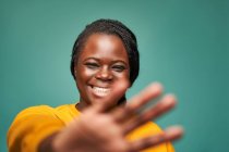 Mujer afroamericana contenta con ropa amarilla demostrando gesto de defensa con brazo extendido contra fondo azul - foto de stock