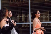 Amis féminines positives dans des lunettes de soleil à la mode et des vêtements décontractés riant joyeusement tout en passant du temps agréable ensemble — Photo de stock