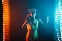 Anonymous astonished ethnic female with open mouth exploring virtual reality in headset on black background — Stock Photo