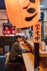 Asiatin in Freizeitkleidung sitzt an Holztheke und wartet auf Bestellung in Ramen-Bar — Stockfoto