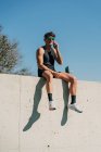 Подходящий спортсмен в спортивной одежде разговаривает по мобильному телефону, отдыхая на заборе после тренировки — стоковое фото