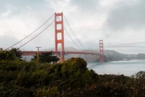 Famous Golden Gate bridge hanging above river with green shore under gloomy gray sky in San Francisco — Stock Photo