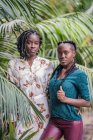 Стильные очаровательные афроамериканские дамы с африканским Брайдом смотрят на камеру в зеленом парке — стоковое фото