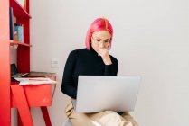Konzentrierte junge Freiberuflerin in lässiger Kleidung sitzt auf einem Stuhl und benutzt Laptop, während sie an einem Projekt in einer leichten modernen Wohnung arbeitet — Stockfoto