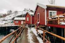 Holzweg in der Nähe einer Barackenmauer in einem Küstenort in der Nähe eines schneebedeckten Bergrückens an einem Wintertag auf den Lofoten, Norwegen — Stockfoto