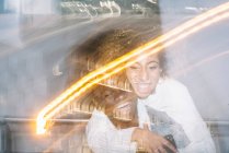 Alegre joven afroamericano macho dando paseo a cuestas a feliz novia con el pelo rizado en traje de moda cerca de luces de congelación - foto de stock