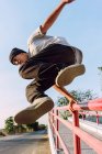 Jovem destemido de baixo ângulo pulando acima do corrimão de metal na cidade enquanto executa acrobacia de parkour no dia ensolarado — Fotografia de Stock