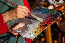 From above of crop unrecognizable senior female painter mixing colors on paint palette in art workshop — Stock Photo
