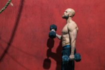 Side view of strong bearded athlete looking away with heavy dumbbells walking in modern gym during weightlifting workout — Stock Photo