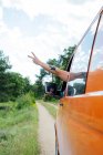 Recorte viajero anónimo conduciendo furgoneta por carretera en el bosque y mostrando señal de paz durante el viaje de verano - foto de stock