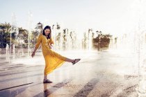 Ganzkörper-Seitenansicht einer fröhlichen Frau in stilvollem Kleid, die das Süßwasser des Emirates Palace Fountain in Abu Dhabi genießt, während sie die Sommerferien in den Emiraten verbringt — Stockfoto