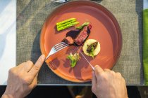 Manos sosteniendo cubiertos onwell plato de lomo de ternera a la parrilla adornado en el restaurante de alta cocina al aire libre - foto de stock