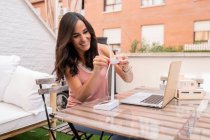 Glad female architect assembling plastic model of windmill while sitting at table with laptop and working on project on terrace — Stock Photo