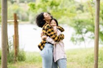 Side view of cheerful multiracial couple of lesbian women embracing in woods and enjoying weekend — Stock Photo