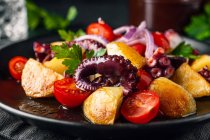 Вкусный салат с осьминогом и разнообразными овощами и травами на столе — стоковое фото