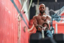 From below strong sportsman pulling rope with heavy weights during intense workout in contemporary gym — Stock Photo