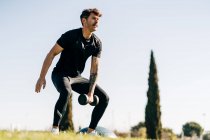 Спортсмен в спортивной форме тренируется с гантелями во время выпада вперед и дышит на лугу в городе — стоковое фото