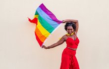 Стильная афроамериканка в модной одежде с красочным флагом, смотрящая в камеру во время празднования — стоковое фото