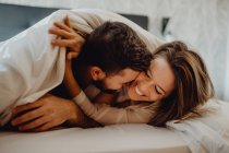 Allegro giovane uomo e donna sorridenti e coccole mentre sdraiati su un comodo letto a casa insieme — Foto stock