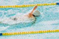 From above back view of unrecognizable paralympic sportsman in goggles and cap without hand swimming crawl style in pool between lanes — Stock Photo