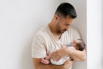 Sanfter Vater steht mit niedlichem schlafenden Säugling an Wand im heimischen Zimmer — Stockfoto