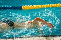 Vista lateral do atleta paralímpico em óculos e boné sem mão nadando rastejar estilo na piscina entre as pistas — Fotografia de Stock