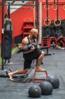 Вид сбоку могучего человека с тяжелым пакетом на табуретке во время функциональной тренировки в современном спортзале — стоковое фото