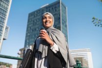 De baixo alegre empresária muçulmana no hijab e com café takeaway em pé na rua — Fotografia de Stock