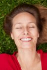 Woman with closed eyes dressed in red lying on the ground in a park with grass — Stock Photo