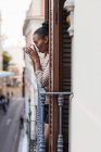 Seitenansicht der reflektierenden Afroamerikanerin mit einer Tasse Heißgetränk, die vom Balkon in der Stadt wegschaut — Stockfoto