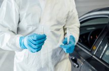 Biologiste avec des gants de protection effectuant un test de coronavirus sur une personne dans une voiture — Photo de stock