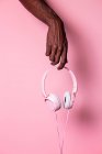 Mão de homem preto anônimo segurando fones de ouvido rosa contra o fundo de cor correspondente — Fotografia de Stock