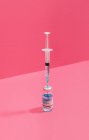 Balão da vacina contra o coronavírus perto da seringa com agulha sobre fundo rosa — Fotografia de Stock